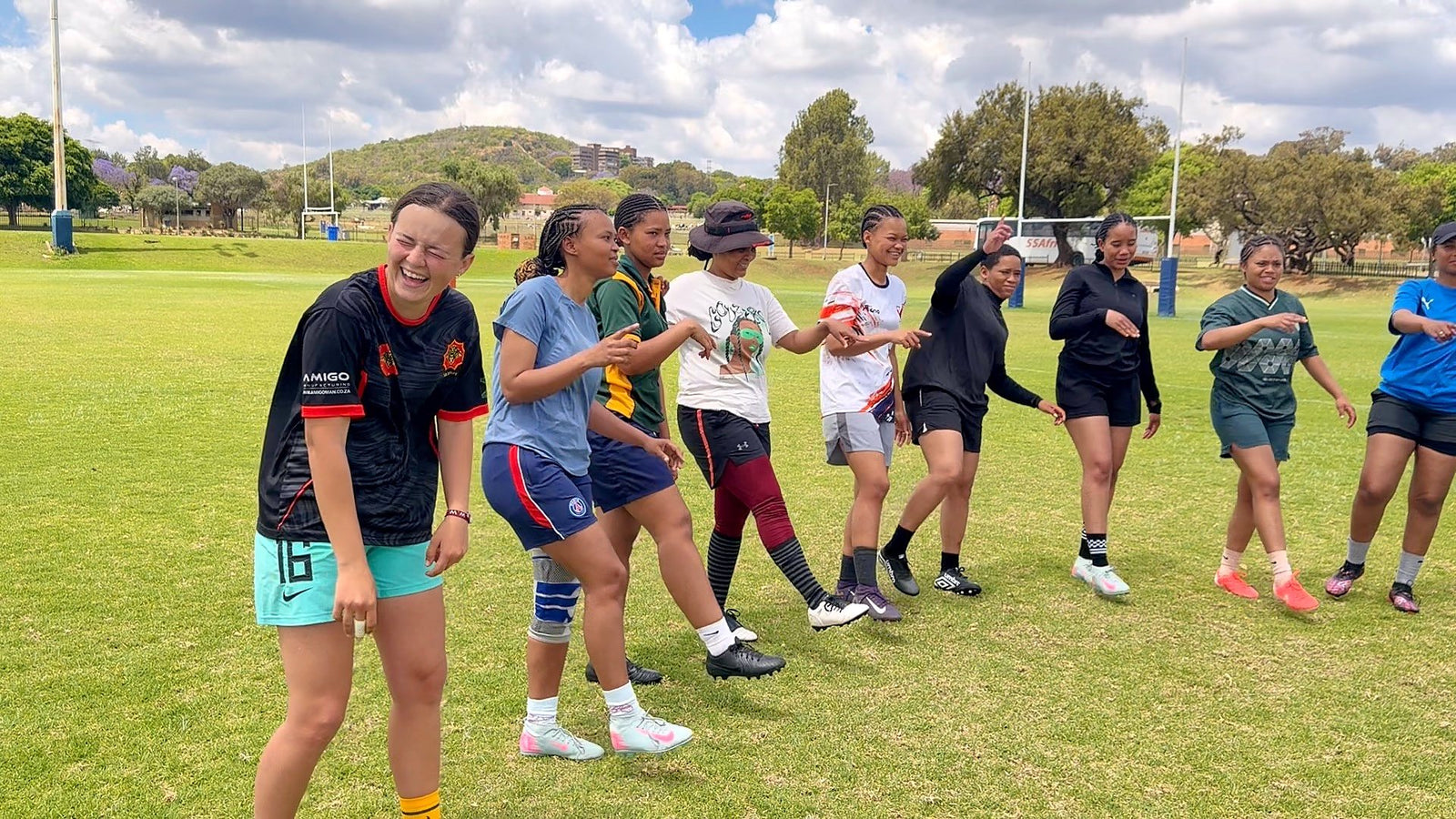 A line of women on a sports field mid-exercise, the nearest one laughing
