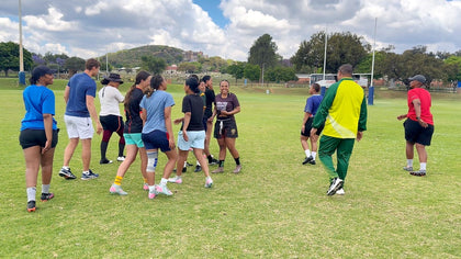 A group of adults standing close together on a field, talking and laughing between exercises